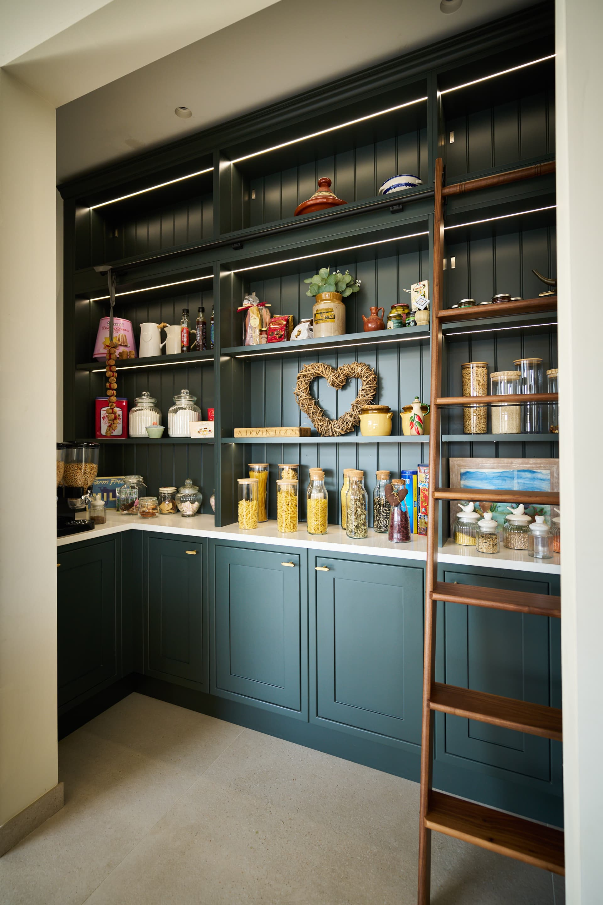 Elegant pantry with teal cabinetry, open shelving with LED lighting, and wooden ladder